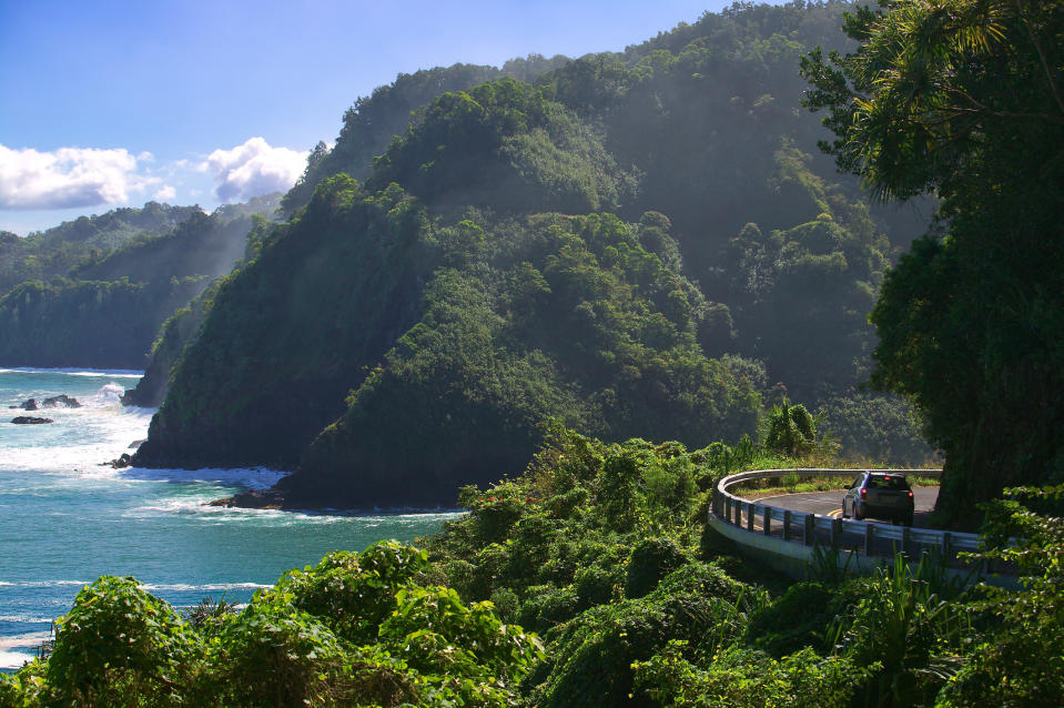 A scenic coastal road winding around a lush green hillside with the ocean in the background