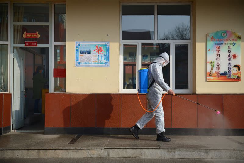 Un trabajador en un traje de protección rocía desinfectante en una escuela secundaria en Hohhot