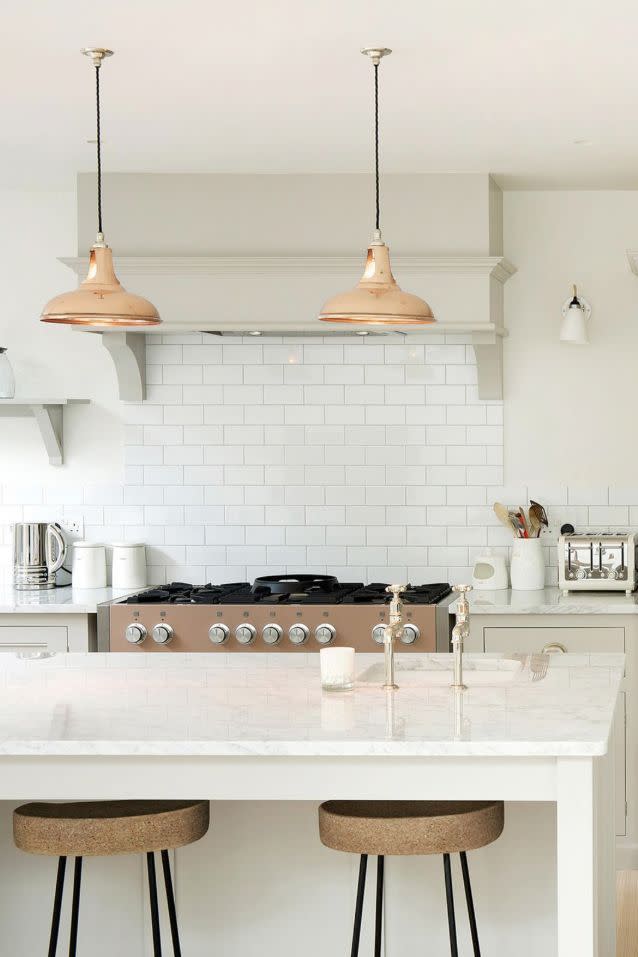 <p>You can get in on minimalism while also sticking to the classics. Take note of this <a href="https://www.devolkitchens.co.uk/" rel="nofollow noopener" target="_blank" data-ylk="slk:deVol kitchen;elm:context_link;itc:0;sec:content-canvas" class="link ">deVol kitchen</a>, for instance. The bronze pendants pair nicely with the kitchen bar stools tucked under the island while also contrasting with the cream trim and glossy white subway tiles.</p>