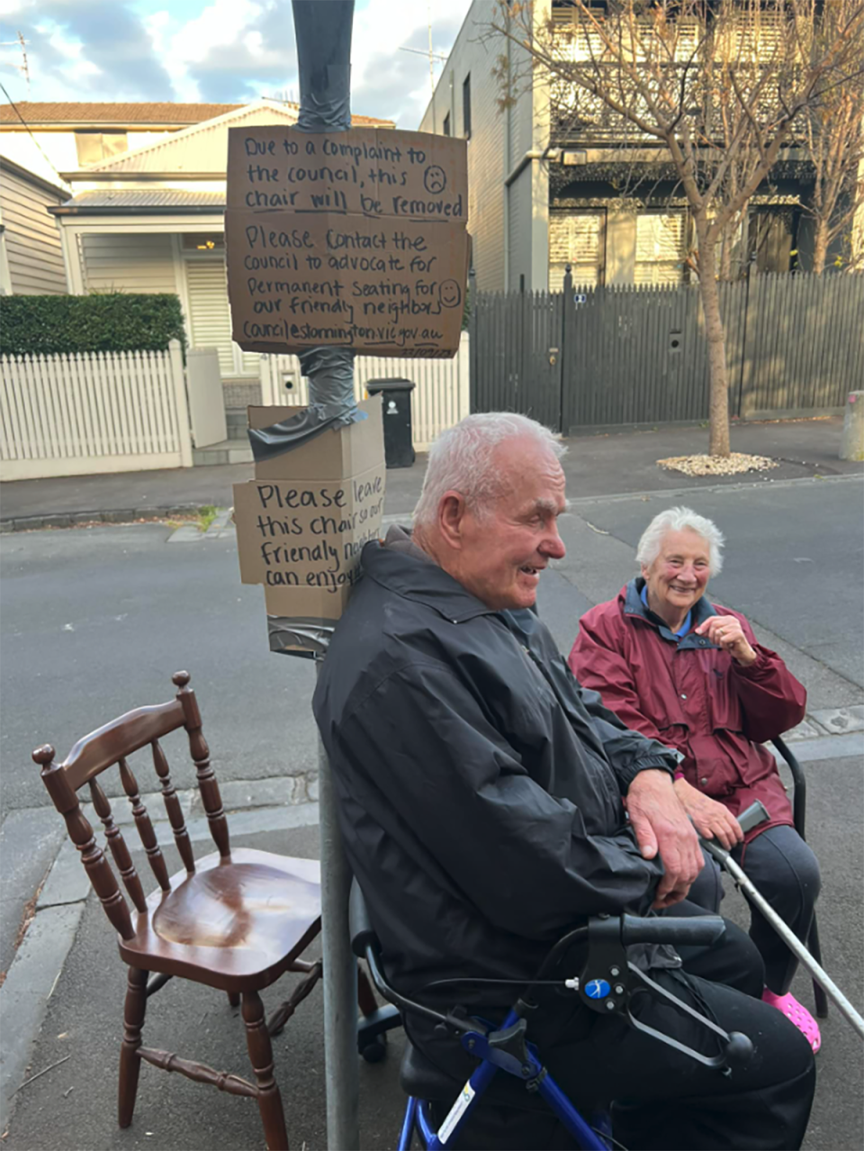 The elderly couple sitting in the chairs provided by locals on Westbourne Street in Melbourne. The cardboard signs can be seen taped to a pole behind them.