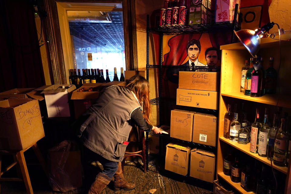 Hanna Cheek clears space on a shelf while organizing storage for wine and liquor in the now-idle performance space at Barbès, a popular neighborhood music venue and bar converted to a bottle shop, Tuesday, Dec. 1, 2020, in New York. (AP Photo/Kathy Willens)
