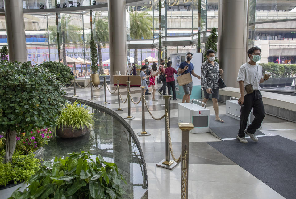 Patrons maintaining physical distance walk through a foot-sanitization bay as they enter the upmarket shopping mall Siam Paragon in Bangkok, Thailand, Sunday, May 17, 2020. Thai authorities allowed department stores, shopping malls and other businesses to reopen from Sunday, selectively easing restrictions meant to combat the coronavirus. (AP Photo/ Gemunu Amarasinghe)