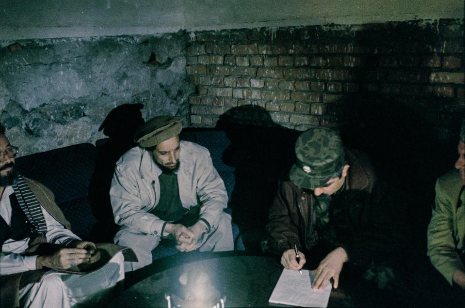 Several men in a dimly lit space are seen signing a document.