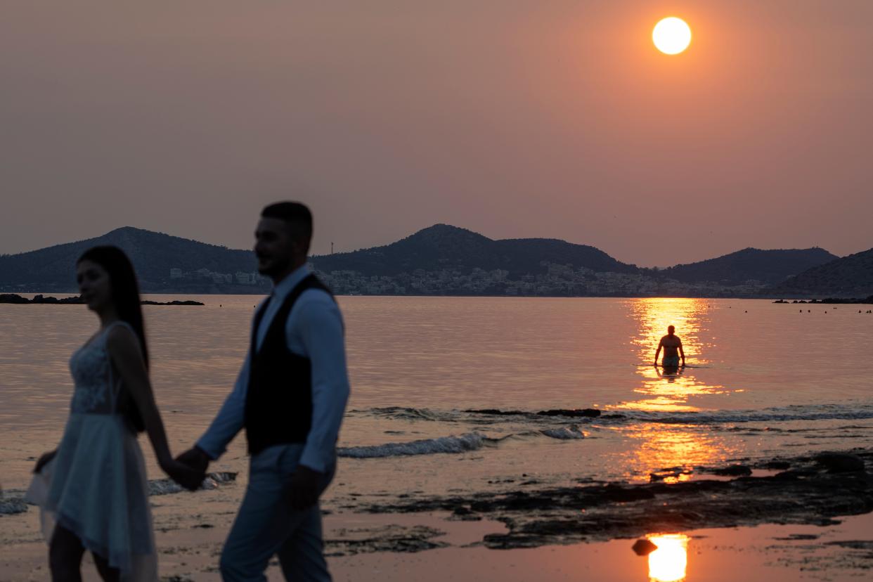A newly married couple poses for photos during sunset as a man takes a dip in the water in Lagonisi southeast of Athens (AP)