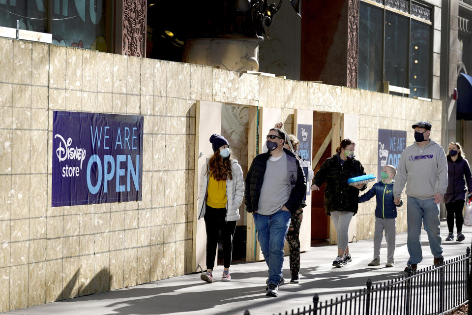 Shoppers pass Saturday, Nov. 28, 2020, an open Disney Store that is still partially boarded up from recent vandalism on Chicago's famed Magnificent Mile shopping district. (AP Photo/Charles Rex Arbogast)