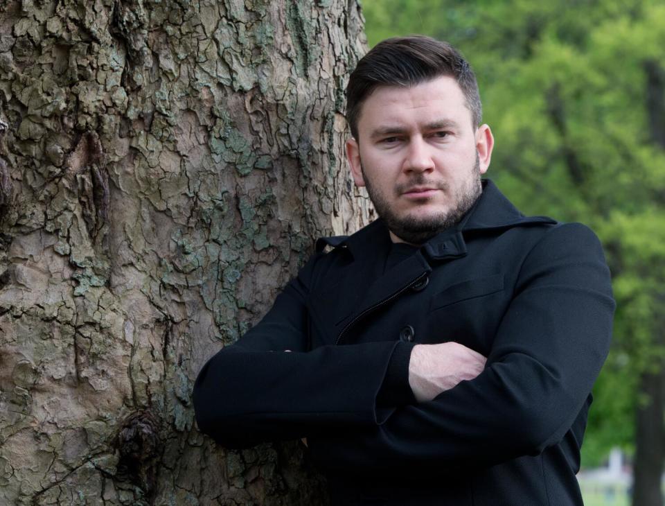 A man stands next to a tree with his arms crossed.