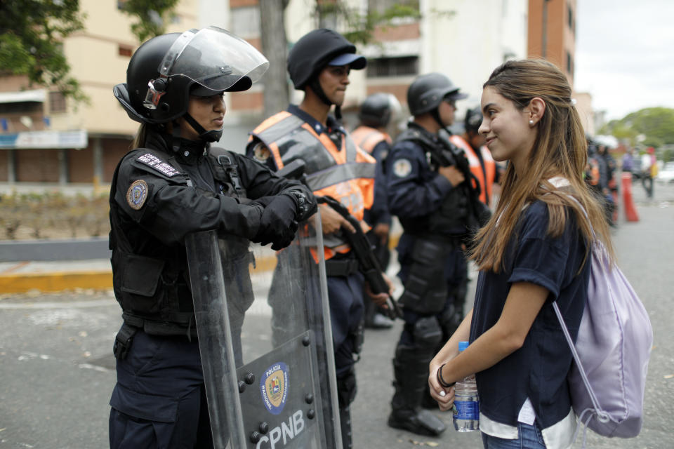 An opponent to Venezuela's President Nicolas Maduro smiles at a riot police officer during a march in Caracas, Venezuela, Saturday, May 4, 2019. Opposition leader Juan Guaido took his quest to win over Venezuela's troops back to the streets calling his supporters to participate in a mobilization outside military installations around the country. (AP Photo/Ariana Cubillos)