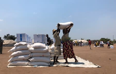 A man helps a woman lift a bag of aid during a distribution for victims of Cyclone Idai at a camp in Guara Guara