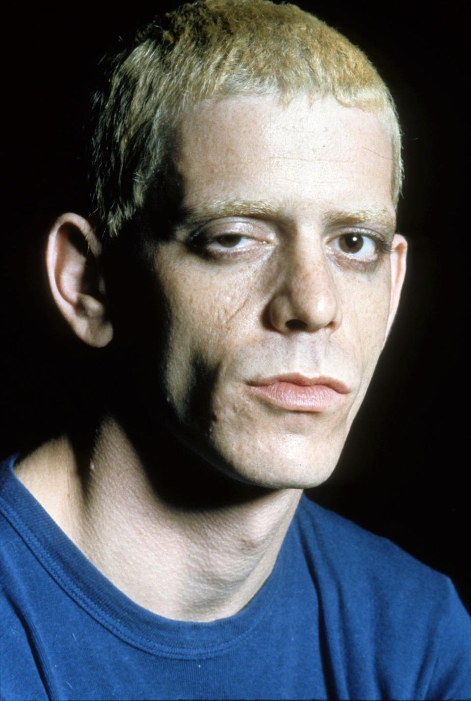 lou reed stares at the camera, he wears a blue shirt