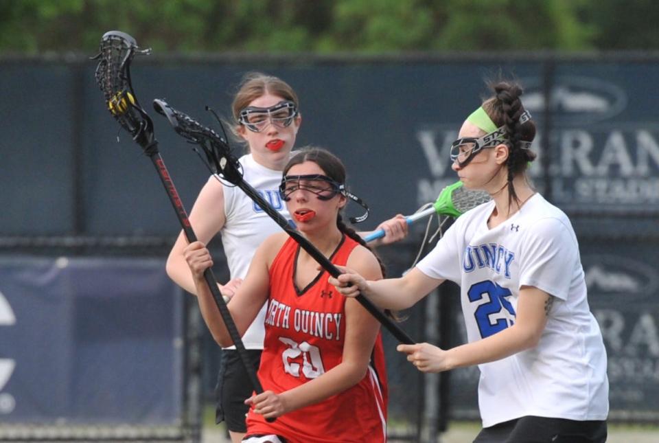 North Quincy's Iris Gjoka, center, tries to elude Quincy defender Lilli Catrambone, right, during girls lacrosse at Veterans Stadium in Quincy, Tuesday, May 16, 2023.