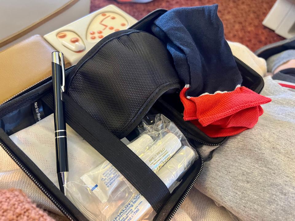 The Tumi kit with navy socks, a black eye mask, a pen, lotion, and toiletries.