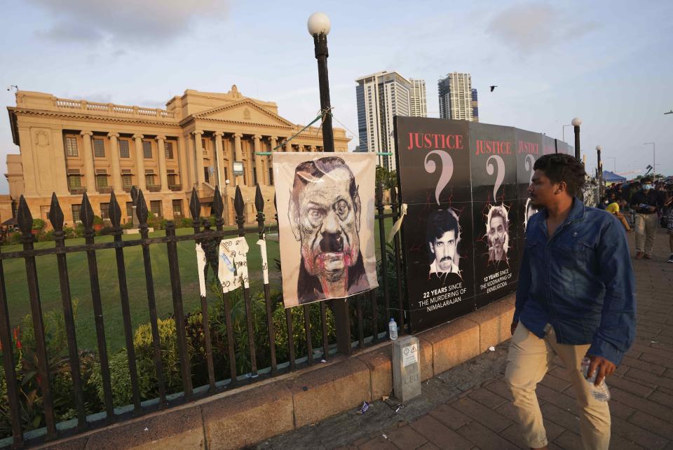 A man walks past a poster that shows a cartooned portrait of prime minister Mahinda Rajapaksa displayed on the fence of president's office during an ongoing protest in Colombo, Sri Lanka, Wednesday, April 20, 2022. Thousands of Sri Lankans have protested outside President Gotabaya Rajapaksa’s office in recent weeks, demanding that he and his brother, Mahinda, who is prime minister, quit for leading the island into its worst economic crisis since independence from Britain in 1948. (AP Photo/Eranga Jayawardena)