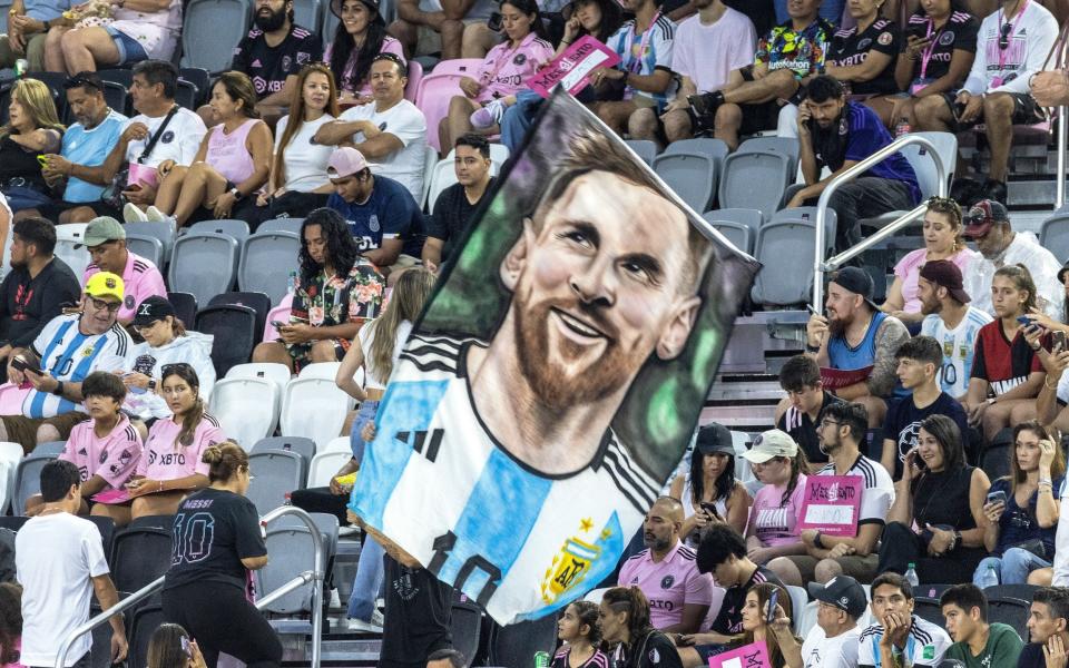 Un fanático del fútbol sostiene una bandera con la imagen del siete veces ganador del Balón de Oro y campeón de la Copa del Mundo, Lionel Messi, durante el evento 'La PresentaSion' organizado por Inter Miami.