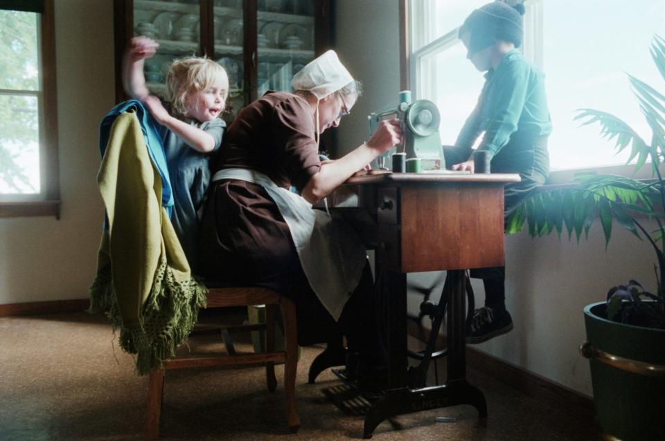 Amish children, not yet school age, watch their mother as she sews with her treadle sewing machine. The Amish in the Shipshewana area of Indiana do not use electricity or gasoline and maintain an austere quality of life with work and church at the heart of their tradition.