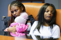 In this Sept. 23, 2021, photo Savannah, left, holds her daughter Chanel, as she sits with her sister Telia, as they listen to their mother Krystal Archie talking during an interview with the Associated Press in Chicago. Archie’s three children were present when police, on two occasions 11 weeks apart, kicked open her front door and tore apart the cabinets and dressers as they executed a search warrant. Archie had never heard of the people they were hunting. (AP Photo/Nam Y. Huh)