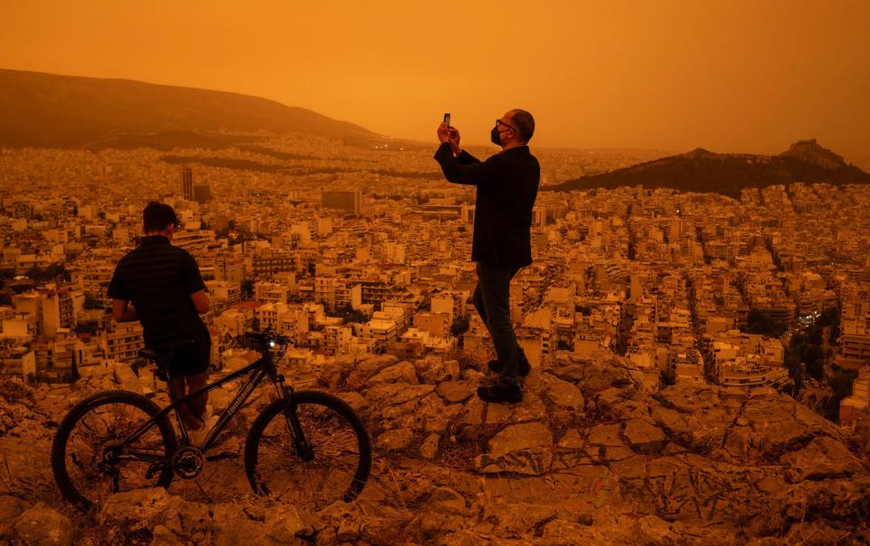 A man takes a photograph of the city of Athens from Tourkovounia hill, as southerly winds carry waves of Saharan dust to the city, in Athens