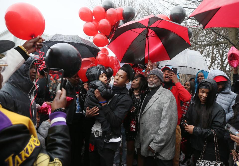 Sam Lamb, center, brother of Imani Tolbert Sr., holds Imani's son and his nephew Imani Jr. as they are surrounded by family and friends during a memorial to mark the one year anniversary of Imani Tolbert Sr.'s shooting death on March 11, 2021 in Akron.