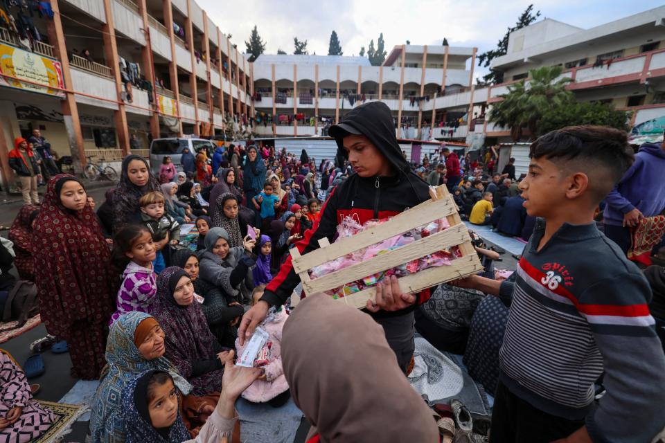 A boy distributes sweets to displaced Palestinians as they attend a special morning prayer to start the Eid al-Fitr festival, marking the end of the holy month of Ramadan, at a school-turned-shelter in Rafah, southern Gaza Strip, on April 10, 2024.