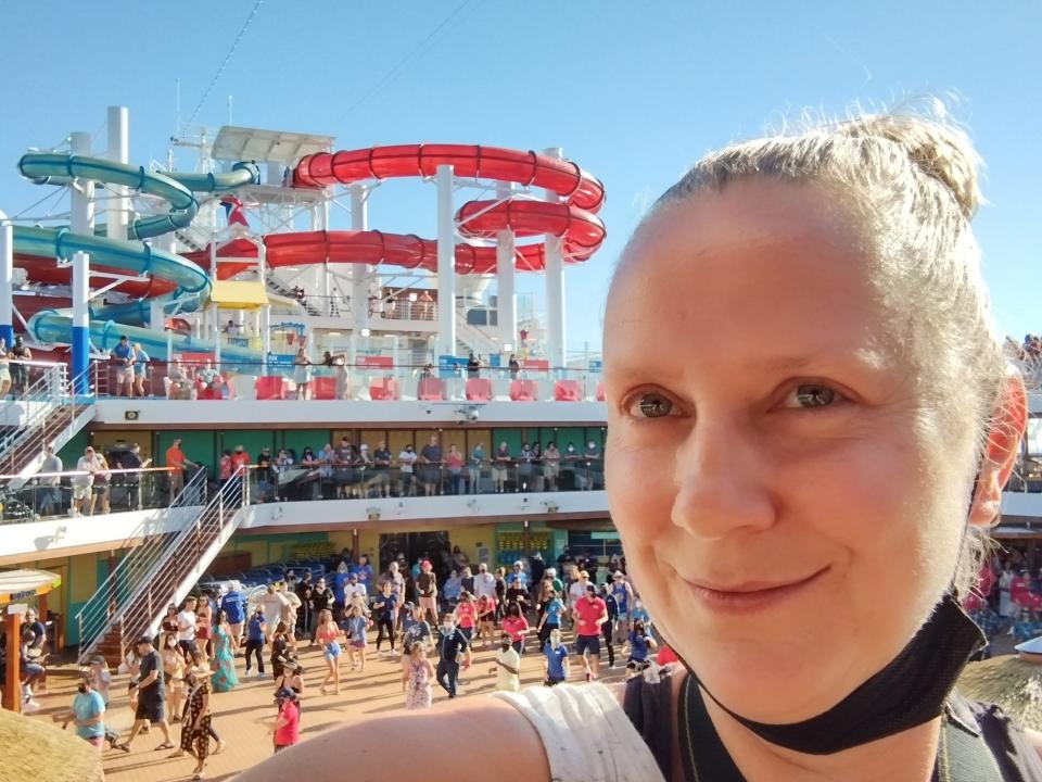 A woman with a mask under her chin takes a selfie in front of a cruise ship waterslide.