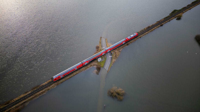 A regional train runs on a rail embankment that is completely surrounded by water. Andreas Arnold/dpa