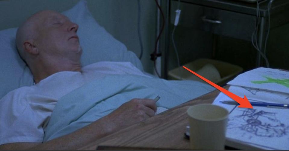 John Kramer laying in hospital bed with his sketchbook on table in front of him in "Saw."