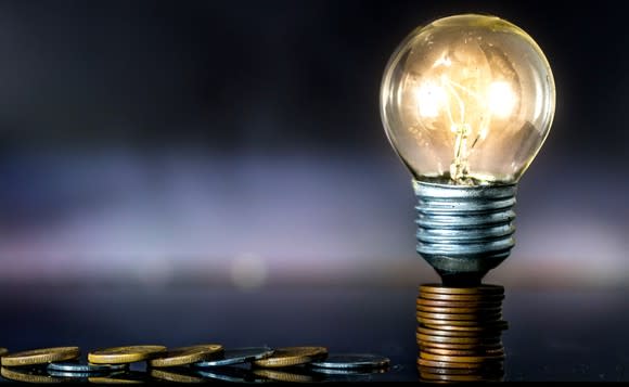 A light bulb sitting on a stack of coins with a trail of coins leading off to the left.