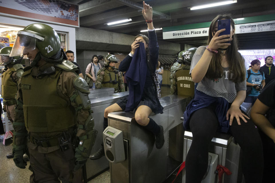 FILE - In this Oct. 18, 2019 file photo, police stand next to students blocking the turnstile to the subway protesting against the rising cost of subway and bus fare, in Santiago. (AP Photo/Esteban Felix, File)