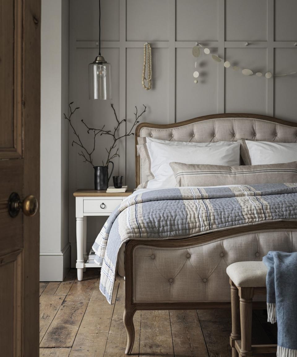 Grey cushioned bed with wooden frame, white bedside table