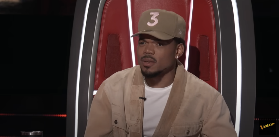 Chance the Rapper in a jacket and cap, sitting in a red chair on 'The Voice'