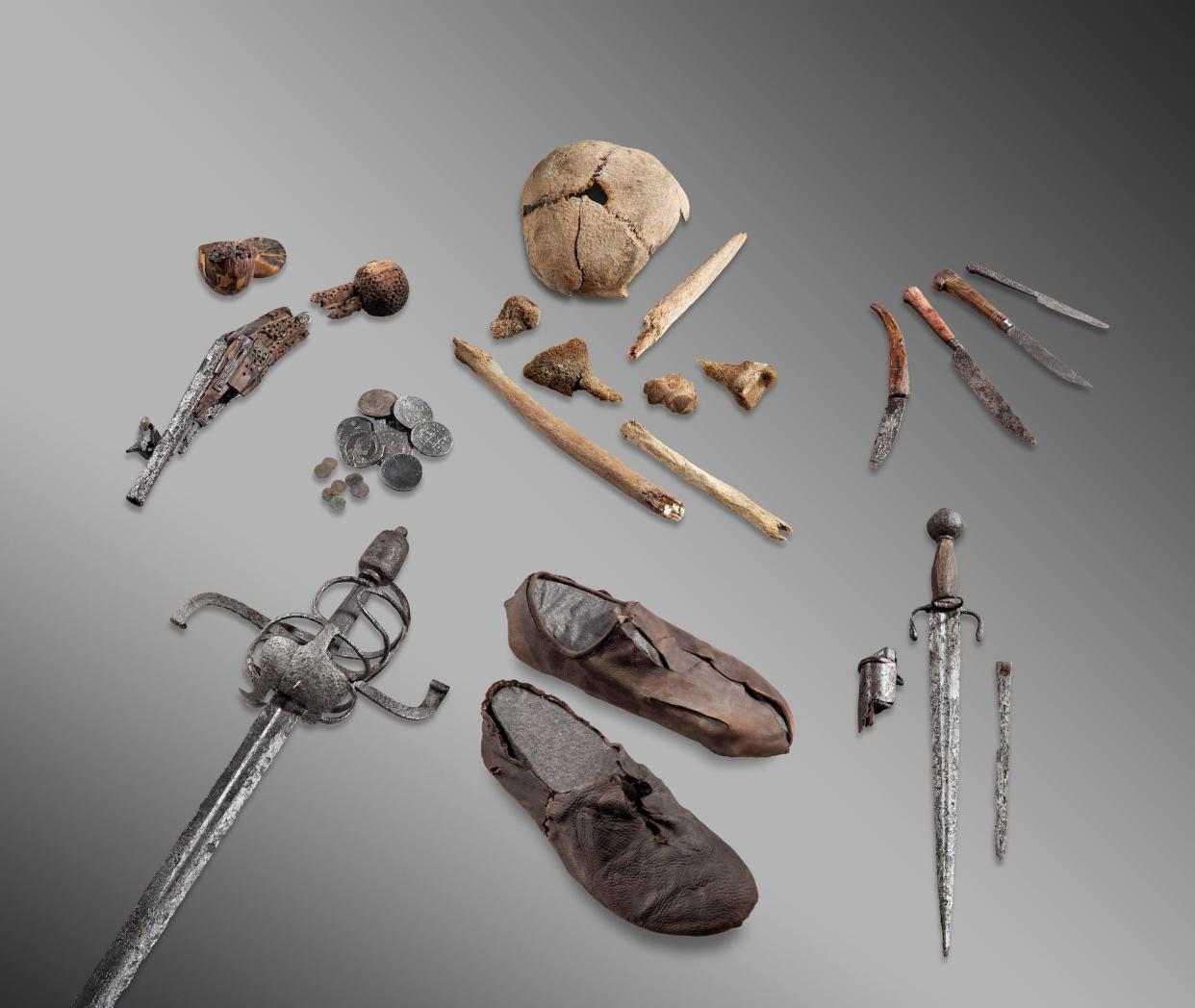 skull cap small bones rusty knives dagger sword coins broken pistol and worn leather shoes spread out on a grey background