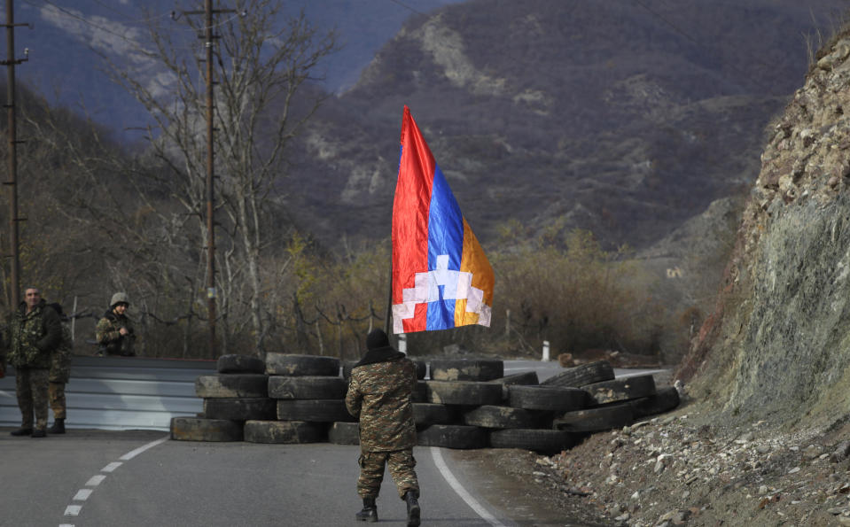 An ethnic Armenian soldier walks with Nagorno-Karabakh's flag towards a checkpoint near village of Charektar in the separatist region of Nagorno-Karabakh at a new border with Kalbajar district turned over to Azerbaijan, Wednesday, Nov. 25, 2020. The Azerbaijani army has entered the Kalbajar region, one more territory ceded by Armenian forces in a truce that ended deadly fighting over the separatist territory of Nagorno-Karabakh, Azerbaijan's Defense Ministry said Wednesday. The cease-fire, brokered by Russia two weeks ago, stipulated that Armenia hand over control to Azerbaijan of some areas its holds outside Nagorno-Karabakh's borders. (AP Photo/Sergei Grits)