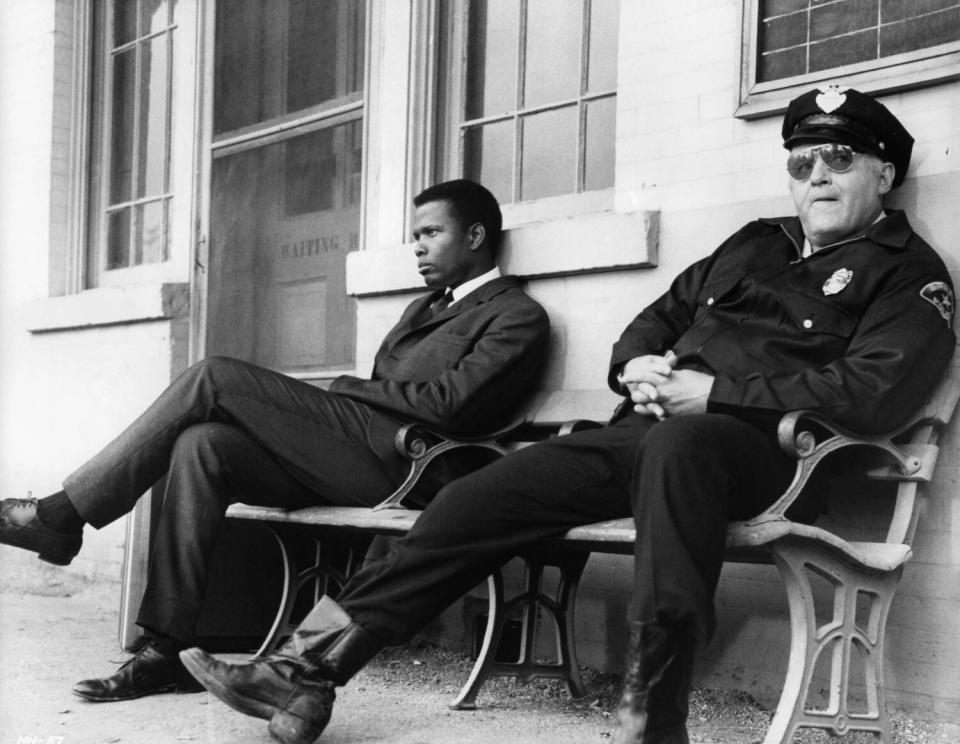 Black man sits on a bench with a police officer in black and white photo