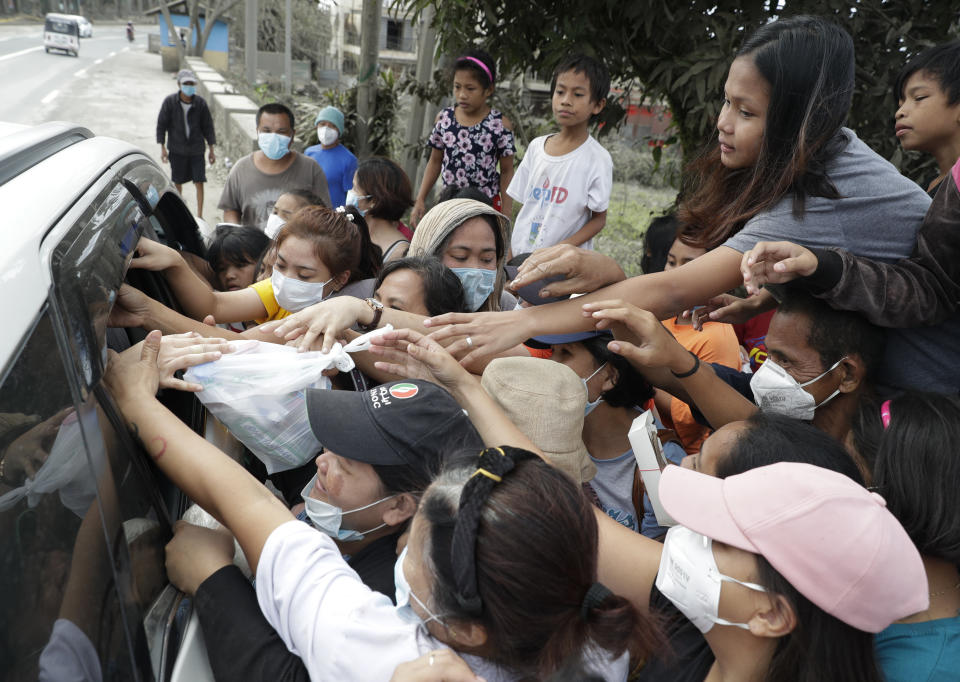 Residents grab relief goods given by a citizen at a town near Taal volcano, Tagaytay, Cavite province, southern Philippines on Sunday Jan.19, 2020. Many poor families living near Taal volcano have been affected due to loss of income after business closures in the area, Philippine officials said Sunday the government will no longer allow villagers to return to a crater-studded island where an erupting Taal volcano lies, warning that living there would be "like having a gun pointed at you." (AP Photo/Aaron Favila)