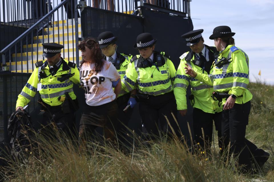 FILE - A Just Stop Oil protester is led away by police and security near the 17th hole during the second day of the British Open Golf Championships at the Royal Liverpool Golf Club in Hoylake, England, July 21, 2023. Climate activists have spraypainted a superyacht, blocked private jets from taking off and plugged holes in golf courses this summer as part of an intensifying campaign against the emissions-spewing lifestyles of the ultrawealthy. (AP Photo/Peter Morrison, File)