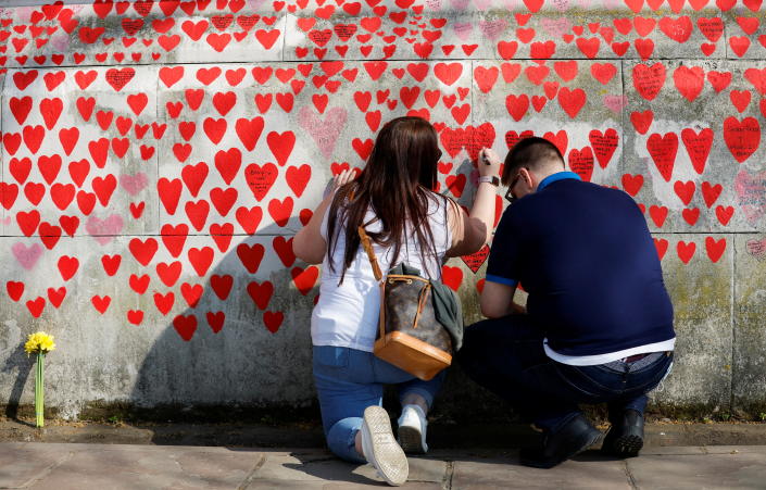 Two people write messages on heart-shaped pieces of paper on the National COVID Memorial Wall.