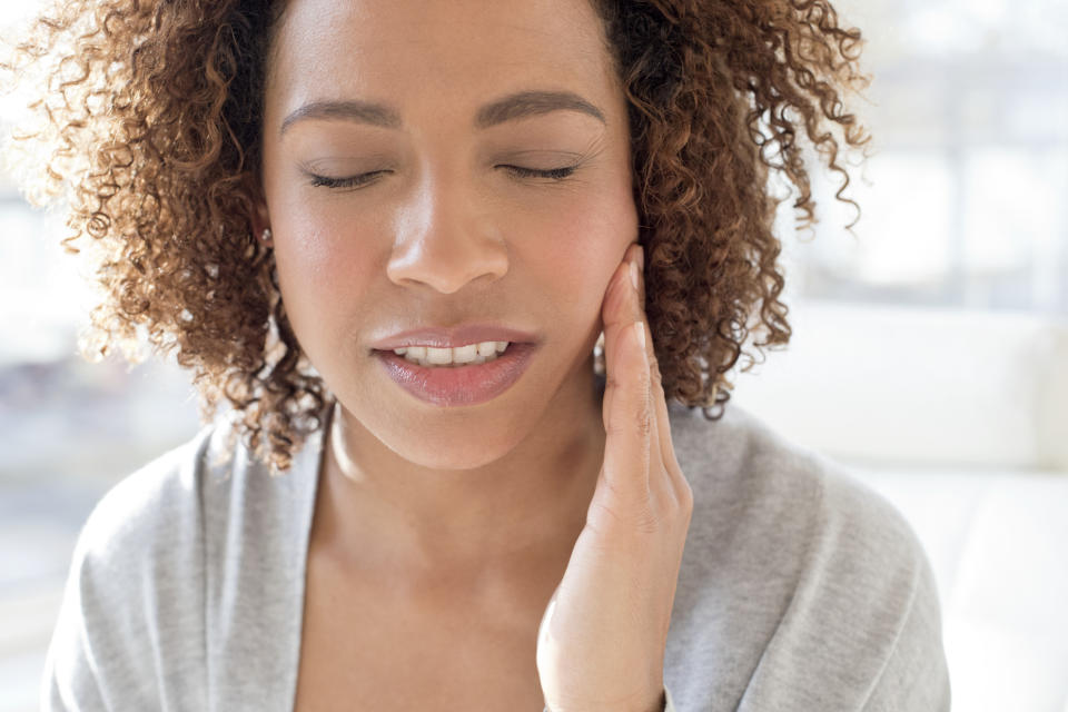 Person with eyes closed touching side of face, appearing to have a toothache or jaw discomfort