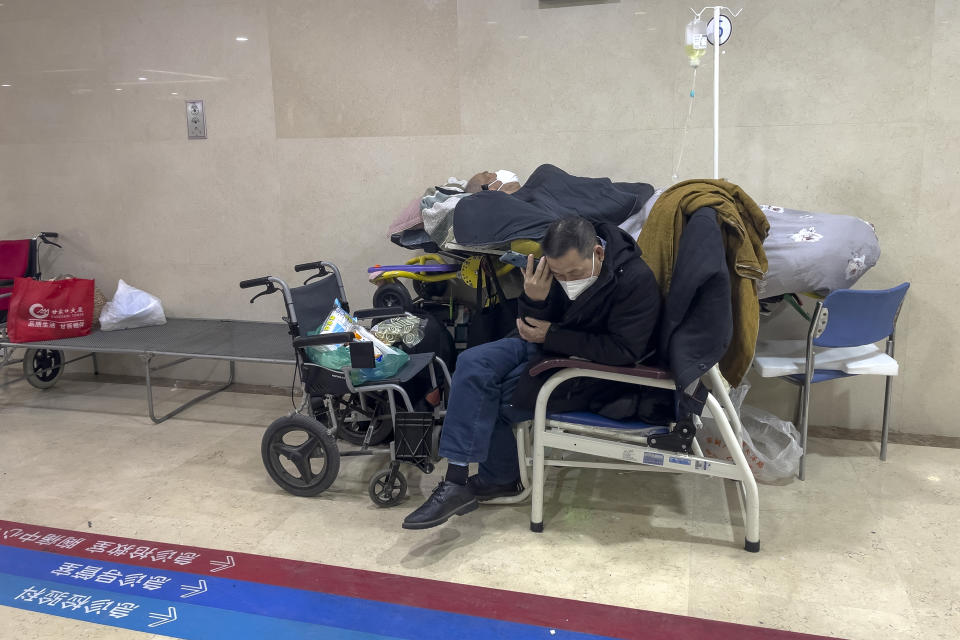A man listens to his phone as he attends to his elderly relative at a corridor of the emergency ward to receive intravenous drips at a hospital in Beijing, Thursday, Jan. 5, 2023. Patients, most of them elderly, are lying on stretchers in hallways and taking oxygen while sitting in wheelchairs as COVID-19 surges in China's capital Beijing. (AP Photo/Andy Wong)