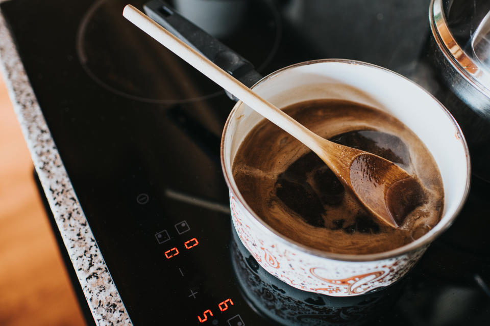 Wooden spoon in a saucepan filled with hot gravy, on an electric hob. Space for copy.