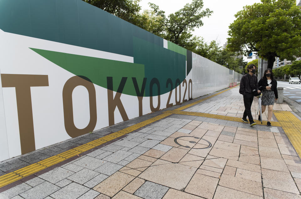 A man and a woman wearing face masks walk along the wall installed to close off a park being prepared for the Olympics and Paralympics Games in Tokyo on Thursday, July 1, 2021. They came to the park only to find out it was shut off. (AP Photo/Hiro Komae)