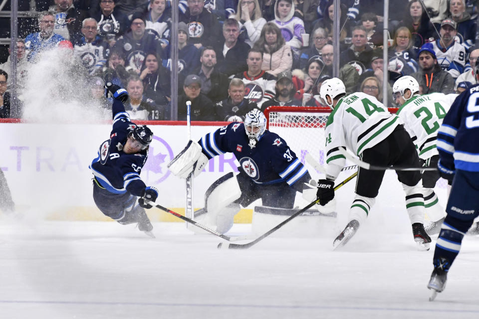 Winnipeg Jets' Mark Scheifele (55) reaches to block a shot by Dallas Stars' Jamie Benn (14) in front of goaltender Connor Hellebuyck (37) during the second period of an NHL hockey match in Winnipeg, Manitoba, on Tuesday, Nov. 28, 2023. (Fred Greenslade/The Canadian Press via AP)