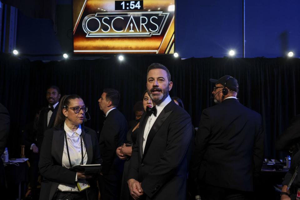 A man in a tux stands under an Oscars sign backstage.