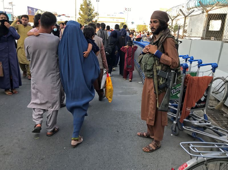 Un miembro de los talibanes monta guardia mientras la gente camina en la puerta de entrada del aeropuerto internacional Hamid Karzai en Kabul