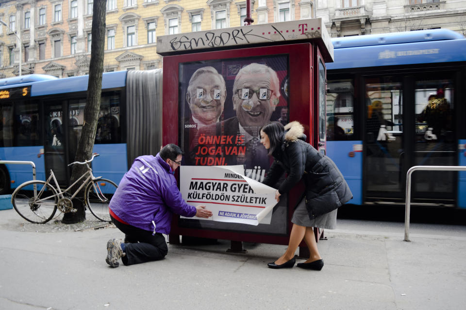 CORRECTS POSITION OF PERSON FROM LEFT TO RIGHT - Katalin Cseh, right, of the Momentum opposition party helps to place a sticker saying "Every sixth Hungarian child is born abroad. Let's not hand over our future," over a poster of the Hungarian government targeting EU Commission President Jean-Claude Juncker and Hungarian-American financier George Soros in Budapest, Hungary, Feb. 26, 2019. The poster reads "You, too, have a right to know what Brussels is preparing to do." The Momentum party's "Reality Campaign" is in response to government ads claiming EU leaders, backed by Soros, are organizing mass migration into Europe. (AP Photo/Pablo Gorondi)