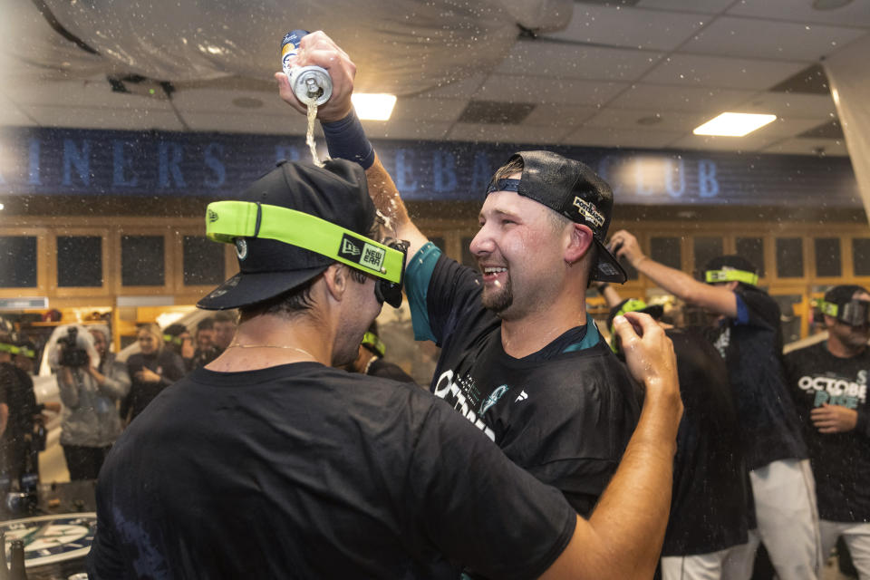 Seattle Mariners' Cal Raleigh, right, celebrates in the clubhouse after the team's baseball game against the Oakland Athletics, Friday, Sept. 30, 2022, in Seattle. The Mariners won 2-1 on a homer by Raleigh to clinch a spot in the playoffs. (AP Photo/Stephen Brashear)