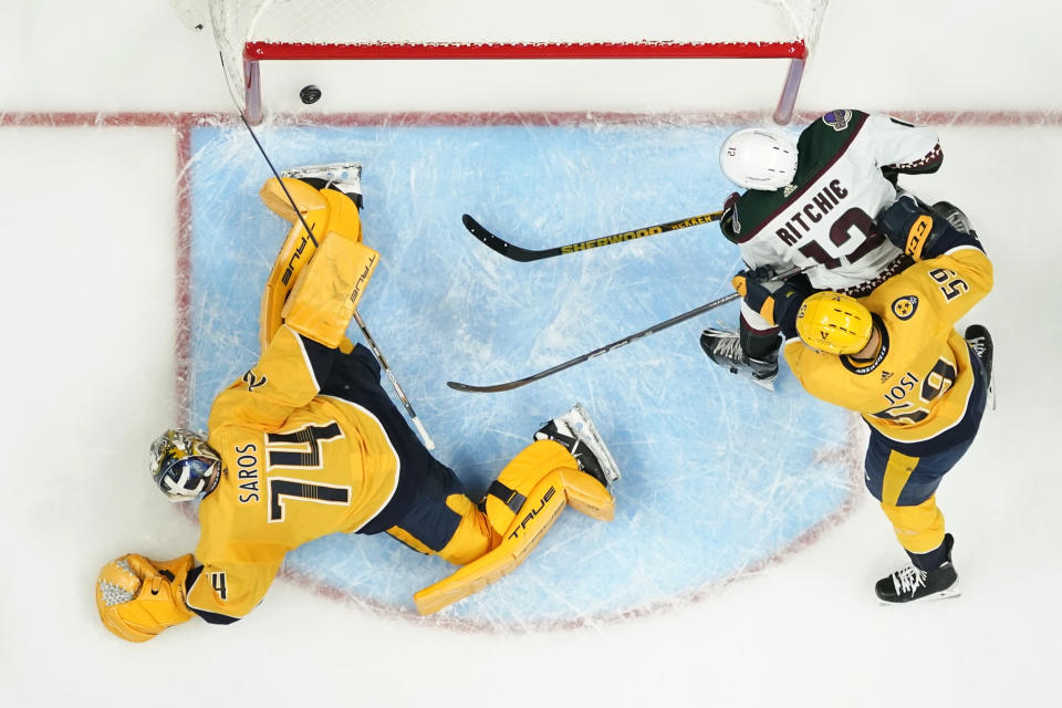 Nashville Predators goaltender Juuse Saros (74) reaches for a goal by Arizona Coyotes' Nick Bjugstad, not shown, in the second period of an NHL hockey game Monday, Nov. 21, 2022, in Nashville, Tenn. Also following the shot are the Coyotes' Nick Ritchie (12) and the Predators' Roman Josi (59). (AP Photo/Mark Humphrey)