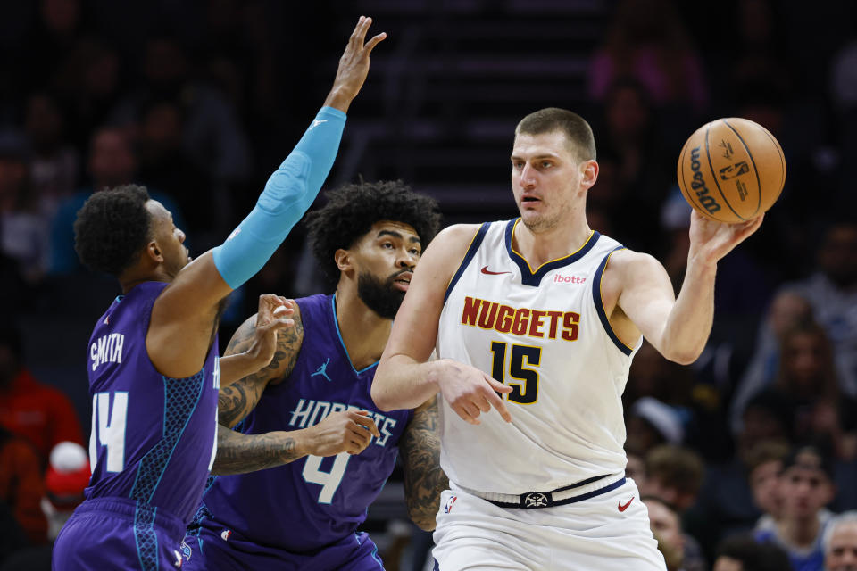 Denver Nuggets center Nikola Jokic (15) looks to pass the ball as Charlotte Hornets guard Ish Smith, left, and center Nick Richards defend during the first half of an NBA basketball game in Charlotte, N.C., Saturday, Dec. 23, 2023. (AP Photo/Nell Redmond)