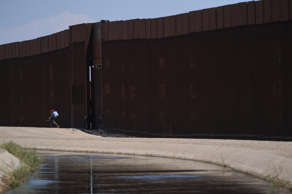 A man walks between a canal carrying water from the Colorado River and a border wall separating San Luis Rio Colorado, Mexico with San Luis, Ariz., on Sunday, Aug. 14, 2022, in San Luis Rio Colorado, Mexico. In November 1922, seven land-owning white men brokered a deal to allocate water from the Colorado River, which winds through the West and ends in Mexico. During the past two decades, pressure has intensified on the river as the driest 22-year stretch in the past 1,200 years has gripped the southwestern U.S.(AP Photo/Gregory Bull)
