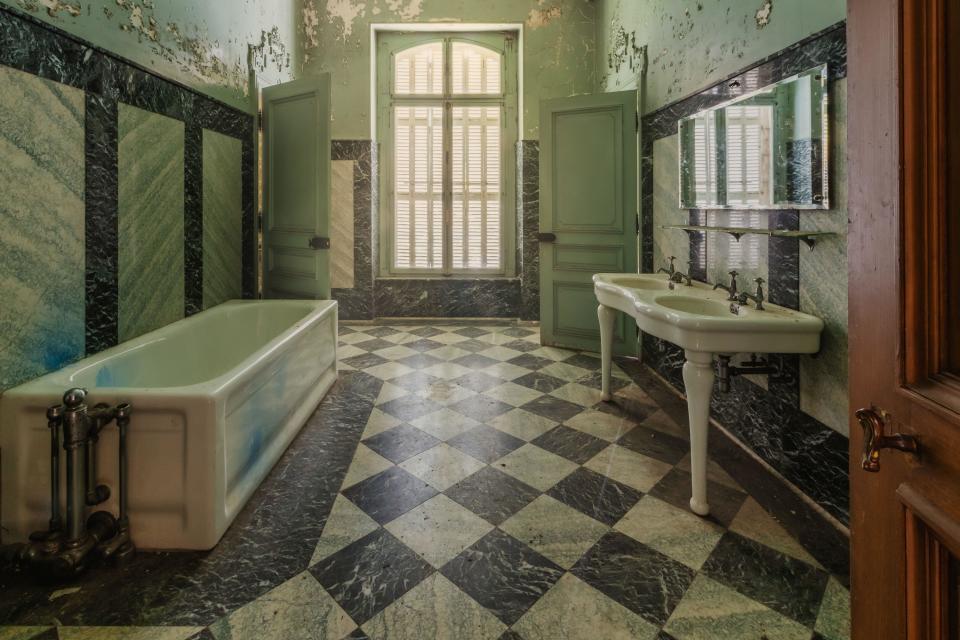 Old historic bathroom with checkerboard pattern on the floor and a large window.