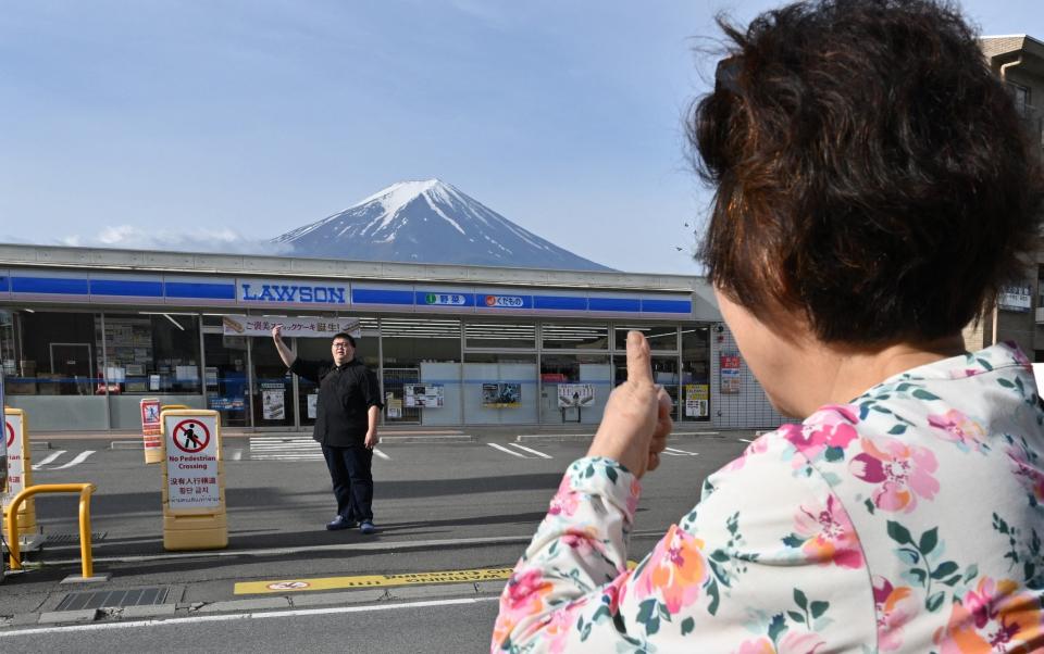 A person takes pictures of Mount Fuji from across the street of a convenience store,
