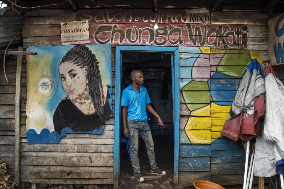 Kagheni, 30, poses in front of his hairdressing salon in Goma, Democratic Republic of Congo, Saturday Nov. 26, 2022. At a time of tension and economic uncertainty, the bold names and brightly colored storefronts bring a sense of normalcy to residents who have contended with conflict and natural disasters such as volcanic eruptions for decades. (AP Photo/Jerome Delay)